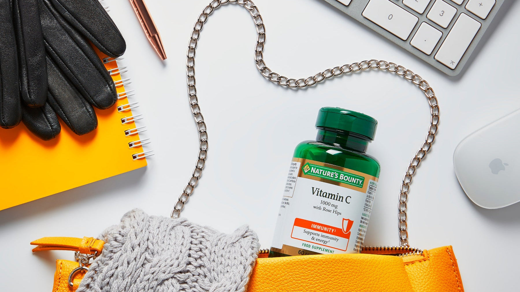 Orange bag with a bottle of Nature's Bounty Vitamin C on a white surface with office supplies.